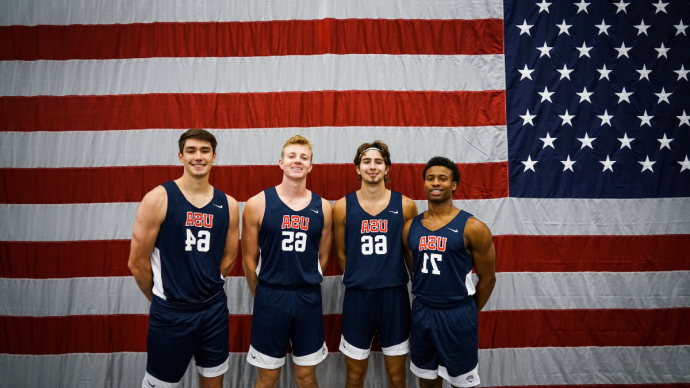 Kaleb Jenkins '22, Tanner Brown '23, AJ Clark '21, and Ben Hanley '21 smile wearing Team USA uniforms in front of an american flag
