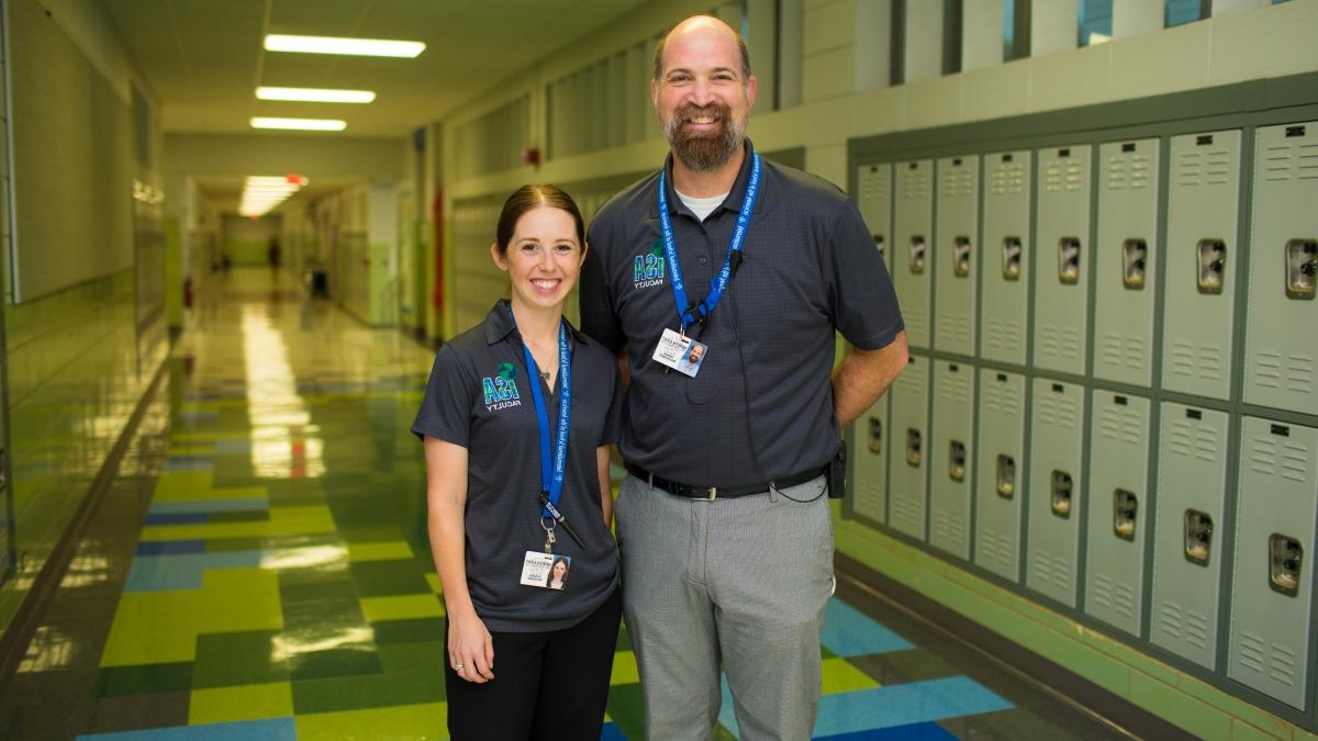 Professor and student stand together in a school hallway